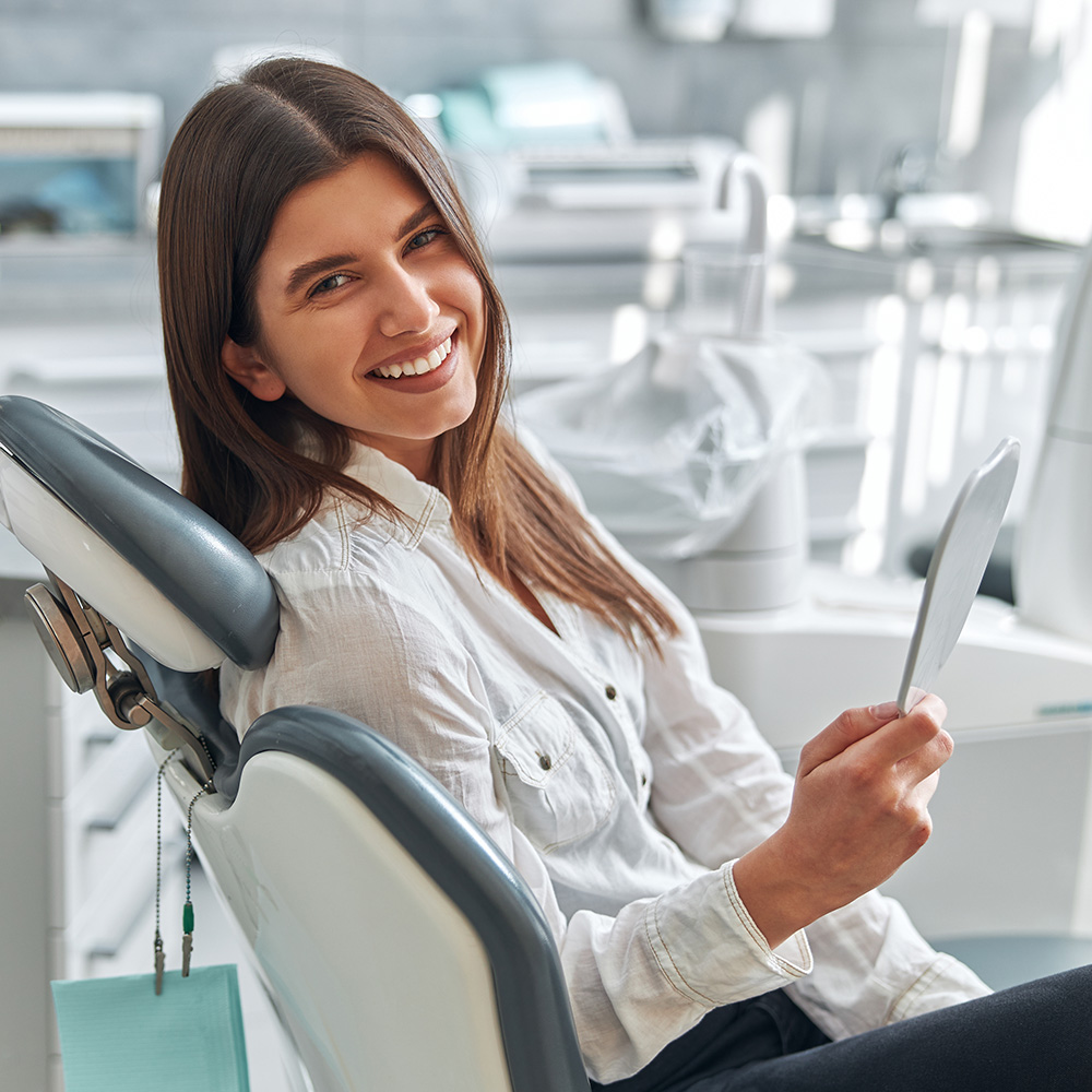 A woman sitting in a dental chair with a tablet in her hand, smiling at the camera.