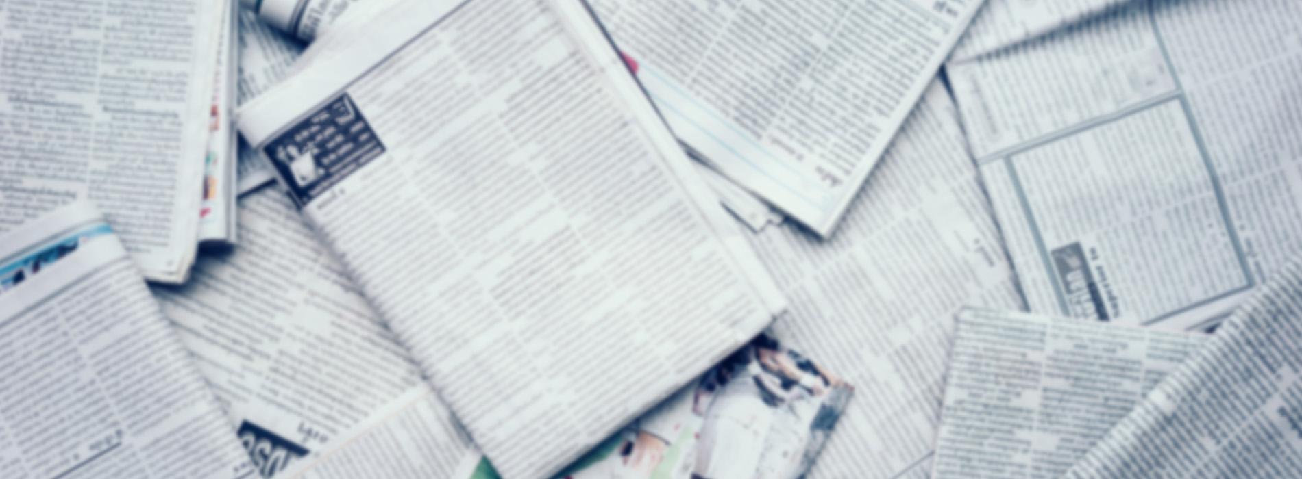 The image shows a collection of newspapers scattered on a surface with a focus on a central area where they are overlapping, creating a sense of disarray or chaos.