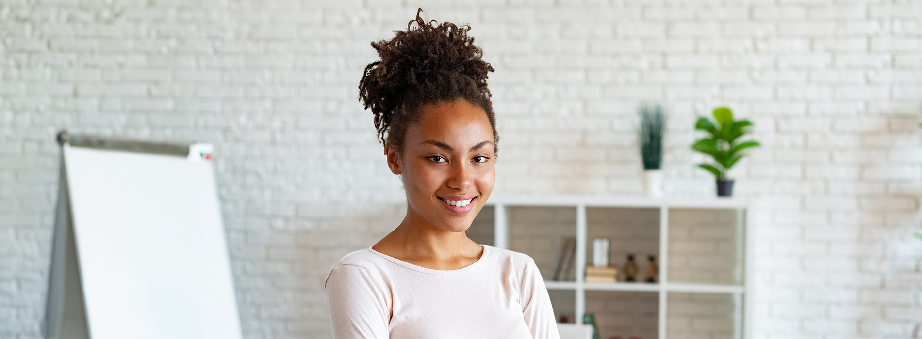 The image is a photograph of a woman with light skin, smiling at the camera. She appears to be in her late twenties or early thirties and has long hair. Her eyes are looking directly at the camera, and she is holding up her index finger near her mouth as if she s making a point or emphasizing something. The background is plain and light-colored, which suggests that this could be a stock photo used for various purposes such as advertising, personal branding, or lifestyle content.