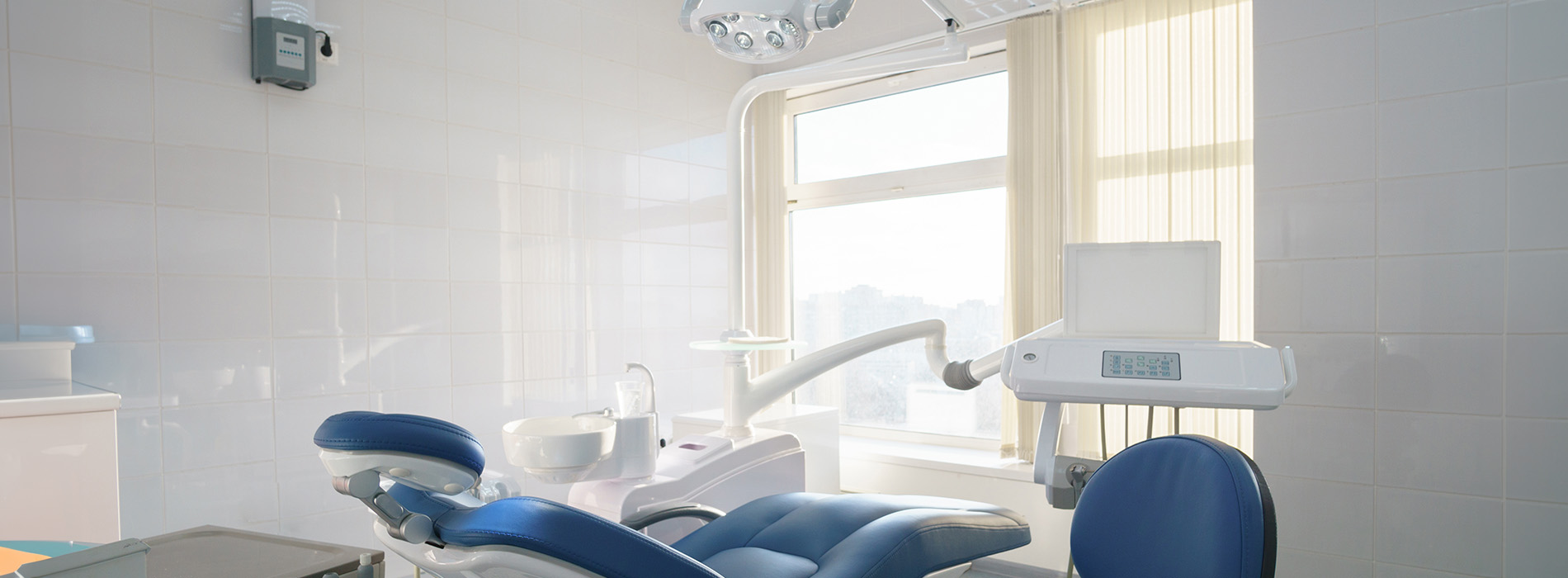 The image shows a modern dental clinic interior with various pieces of equipment, including a dental chair and an X-ray machine.