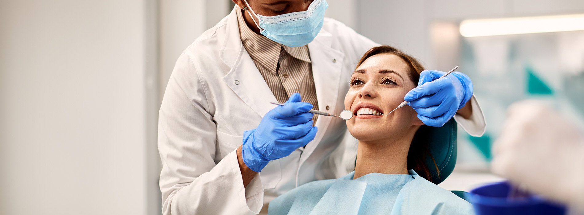 A person is seated in a dental chair, receiving care from a dental professional who stands behind them.