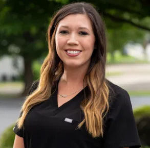 The image shows a woman wearing a black shirt with a name tag, standing outdoors during the daytime.