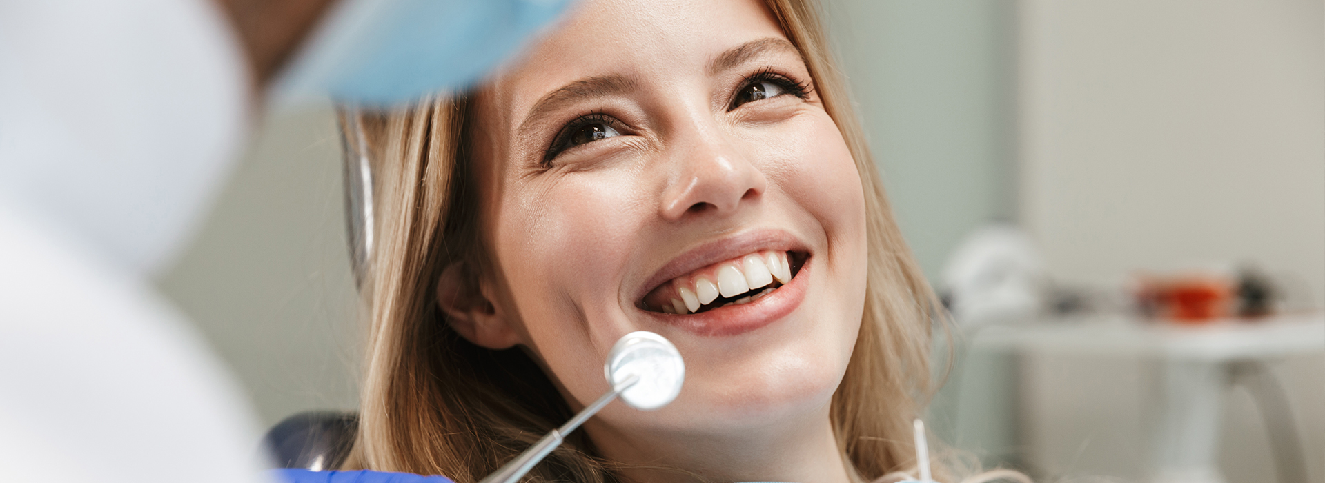 The image shows a woman sitting in front of a dental chair, with a dentist and dental equipment in the background.