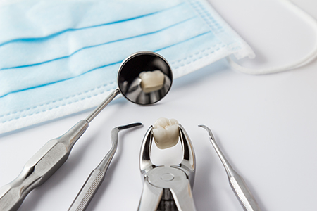 The image shows a set of dental tools, including a drill and a small cup containing a tooth filling, placed on top of a blue cloth with a hole cut out for accessibility purposes.