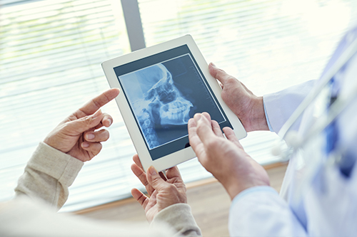 In the image, two people are holding tablets displaying an X-ray image, with a medical professional standing behind them, examining the X-ray alongside the individuals.